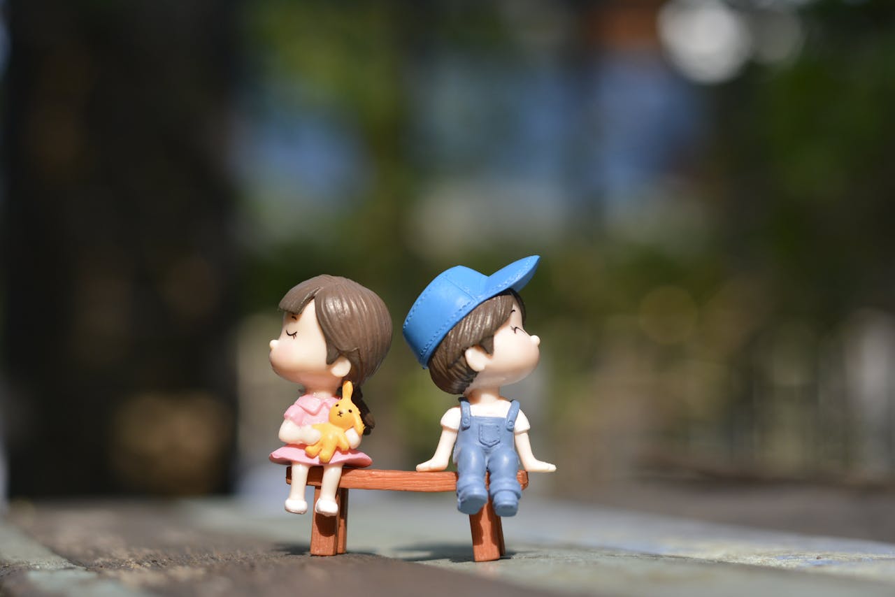 Terapias Adorable figurines of a boy and girl sit on a bench, bathed in summer sunlight.